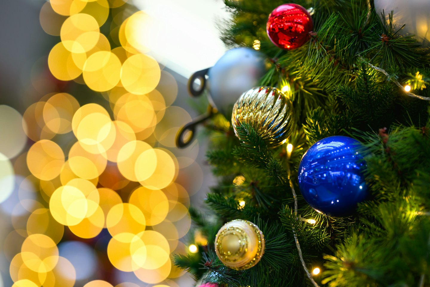 Colorful holiday ornaments hang from a decorated Christmas tree branch.