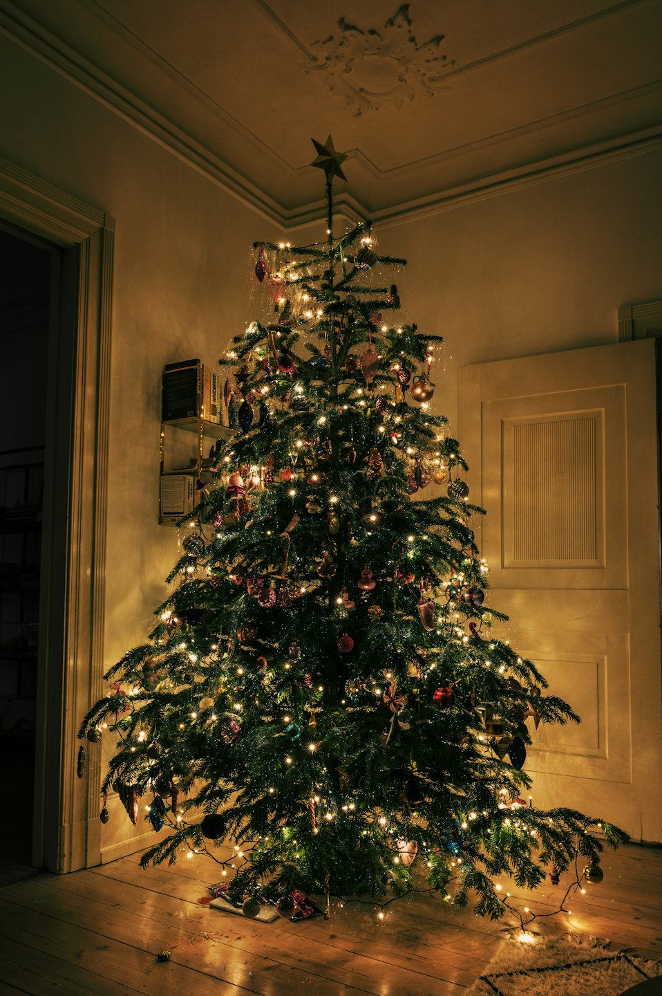 A decorated Christmas tree with warm lights glows in a room.