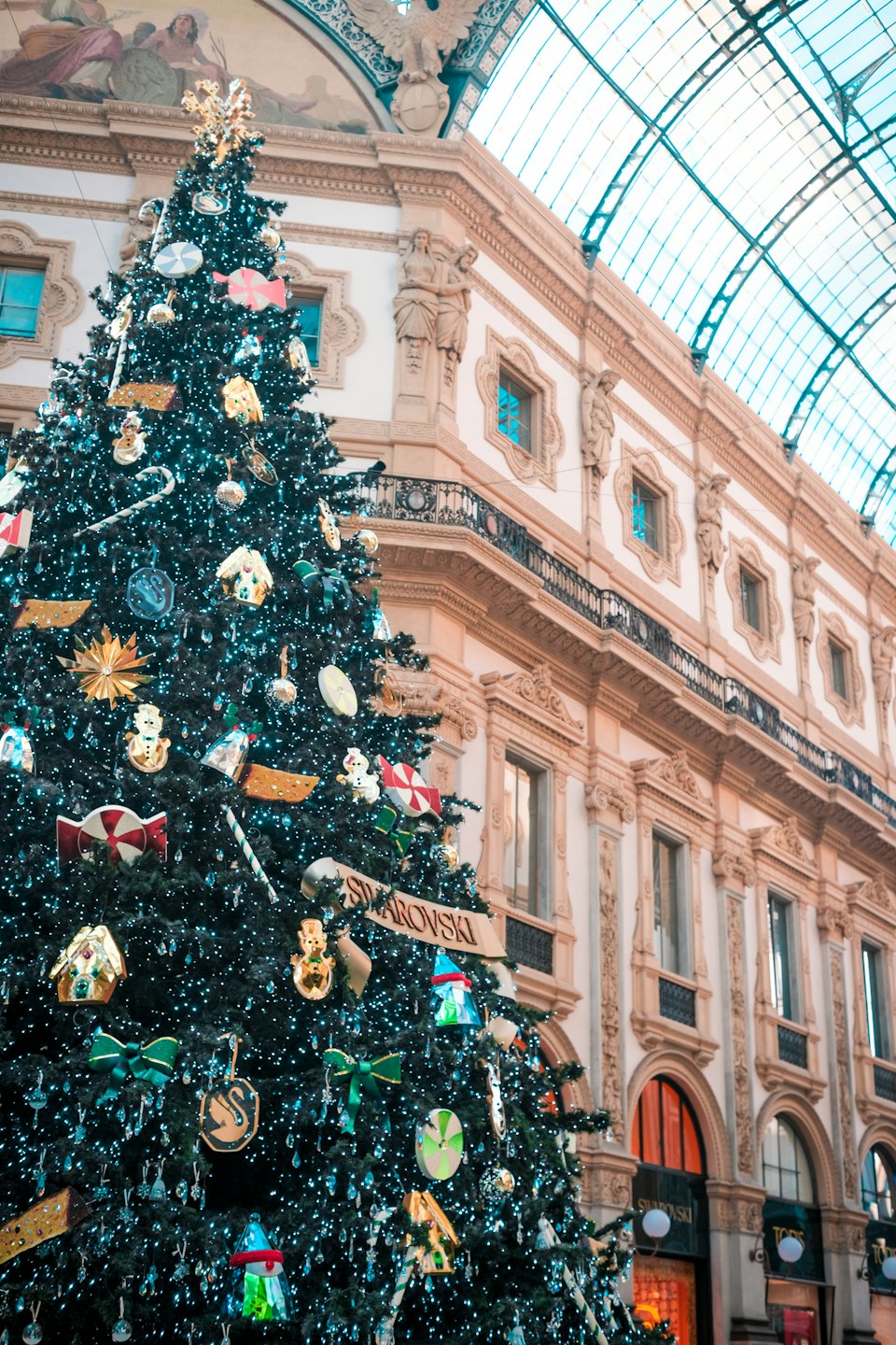 Ornate Christmas tree inside a grand hall with glass roof.